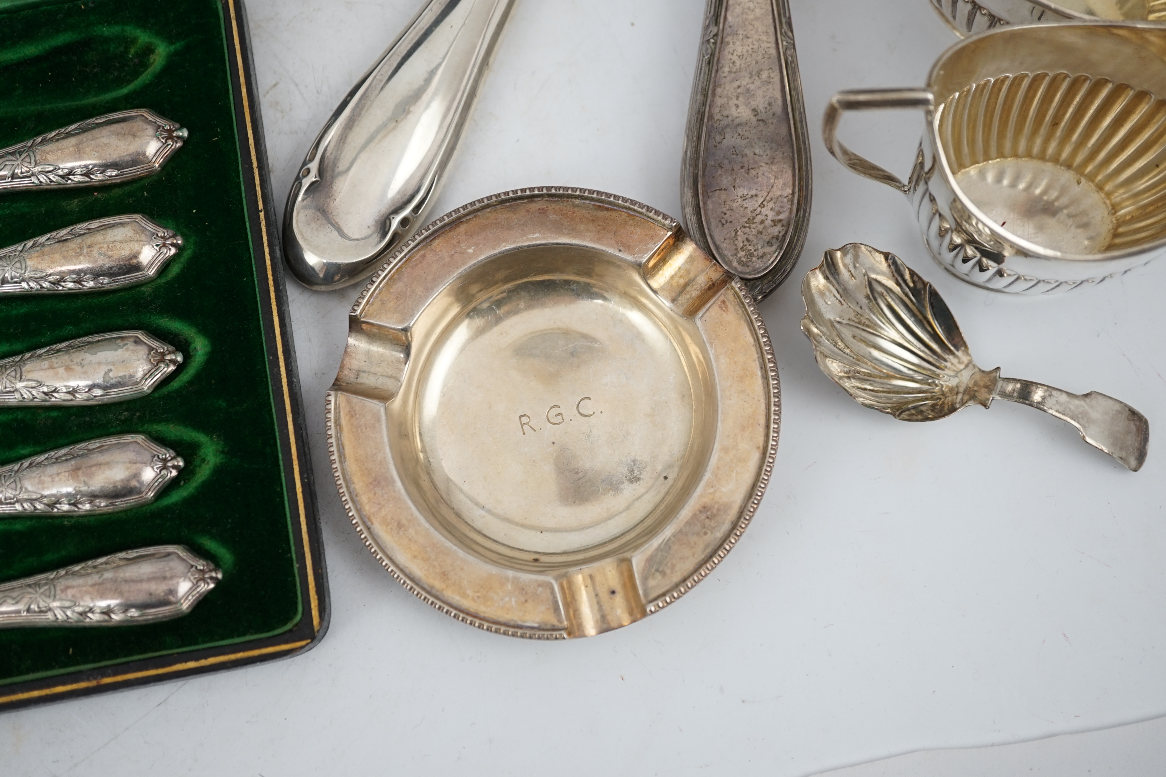 A cased set of twelve George V silver teaspoons with sugar tongs, Sheffield, 1912, two silver hand mirrors, a silver sugar bowl and cream jug, a silver ashtray, a George III silver caddy spoon and cased plated tea knives